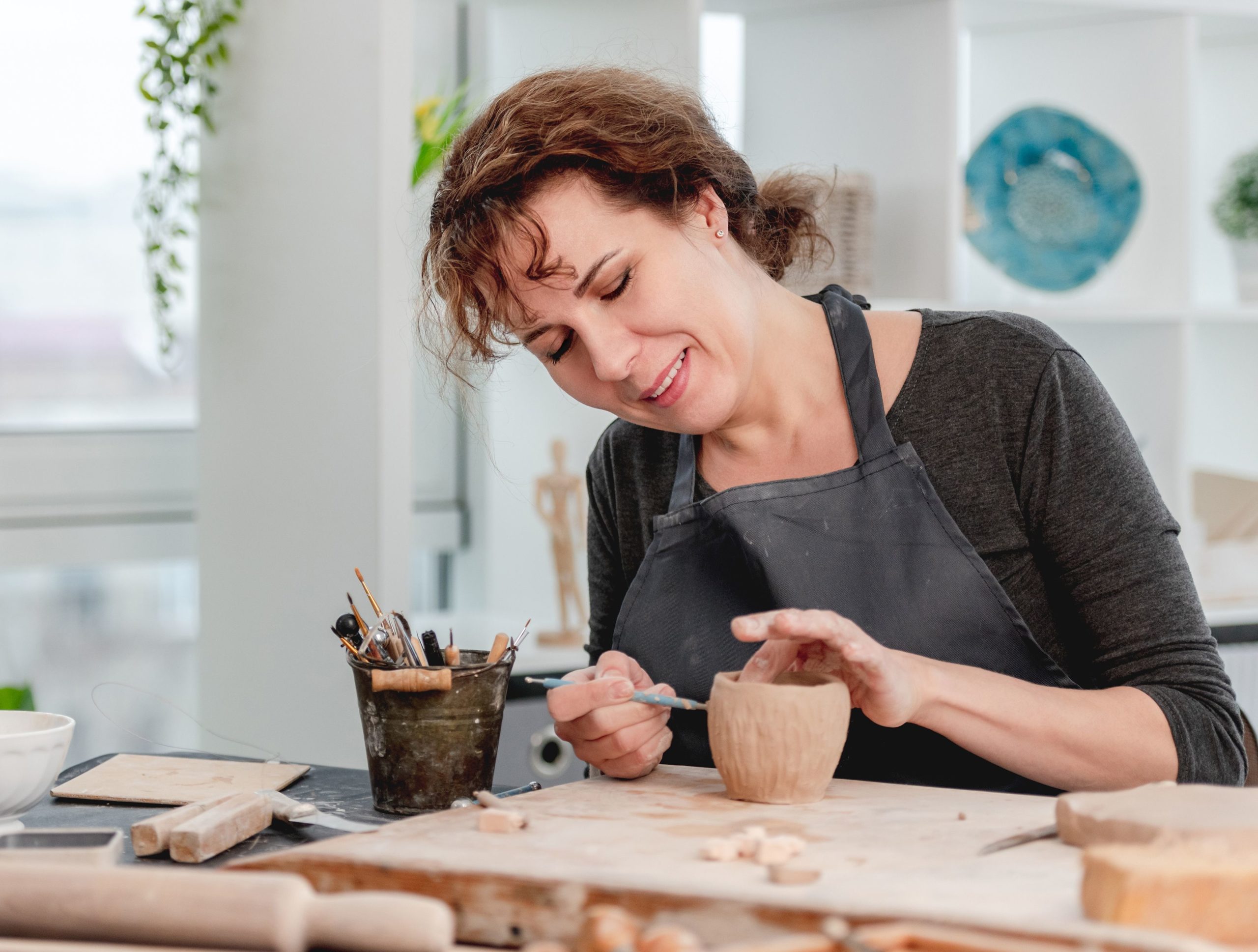 A woman smiles as she creates pottery.