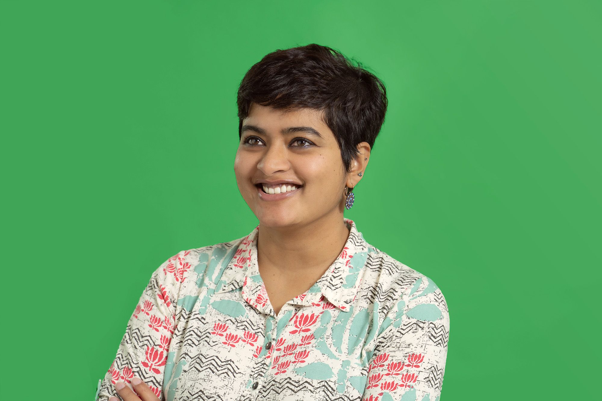Shrutika Gunanayagam has short dark hair and brown eyes. She smiles as she stands in front of a bright green background.