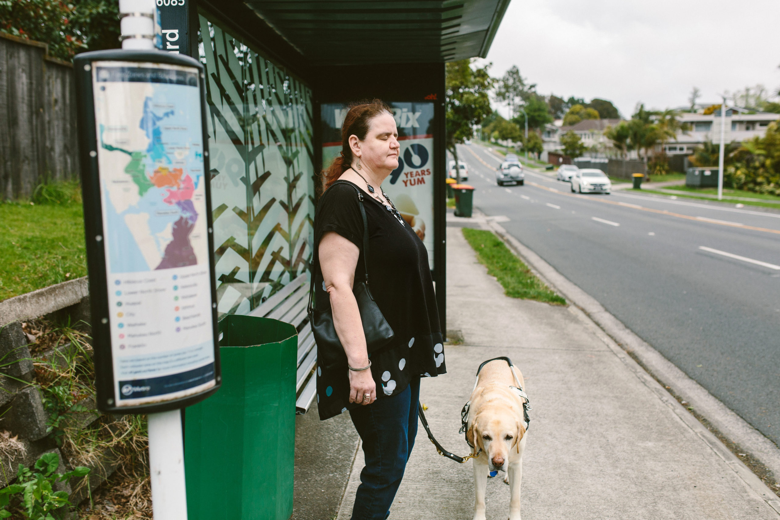 Martine and her guide dog stand by a bus shelter.