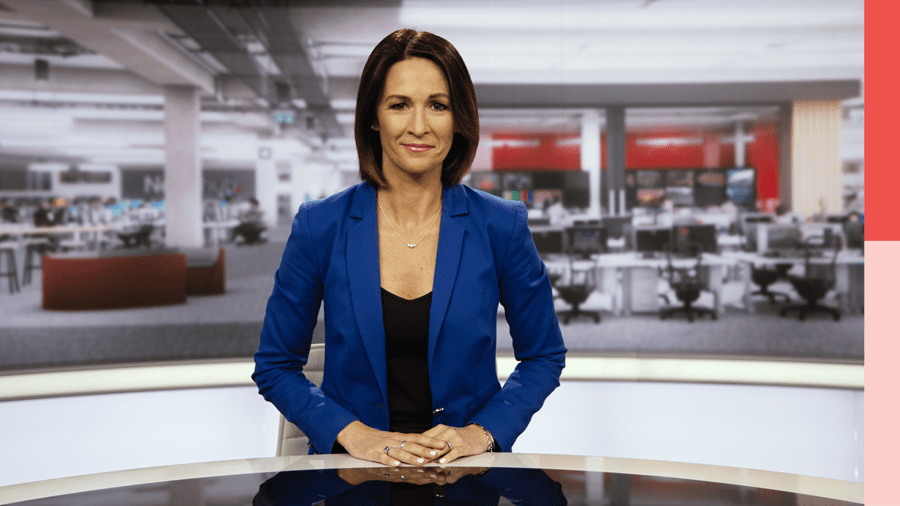 Sacha McNeil sits in a reporting studio wearing a suit.