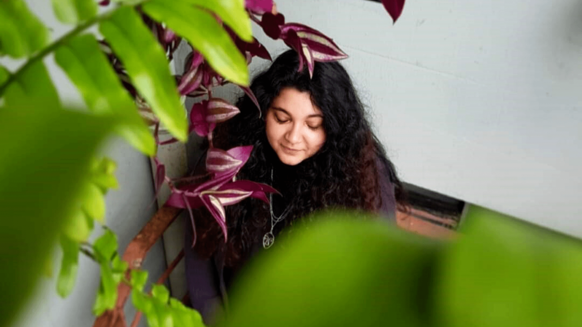 Jennifer has long curly hair, and sits in a botanical garden.