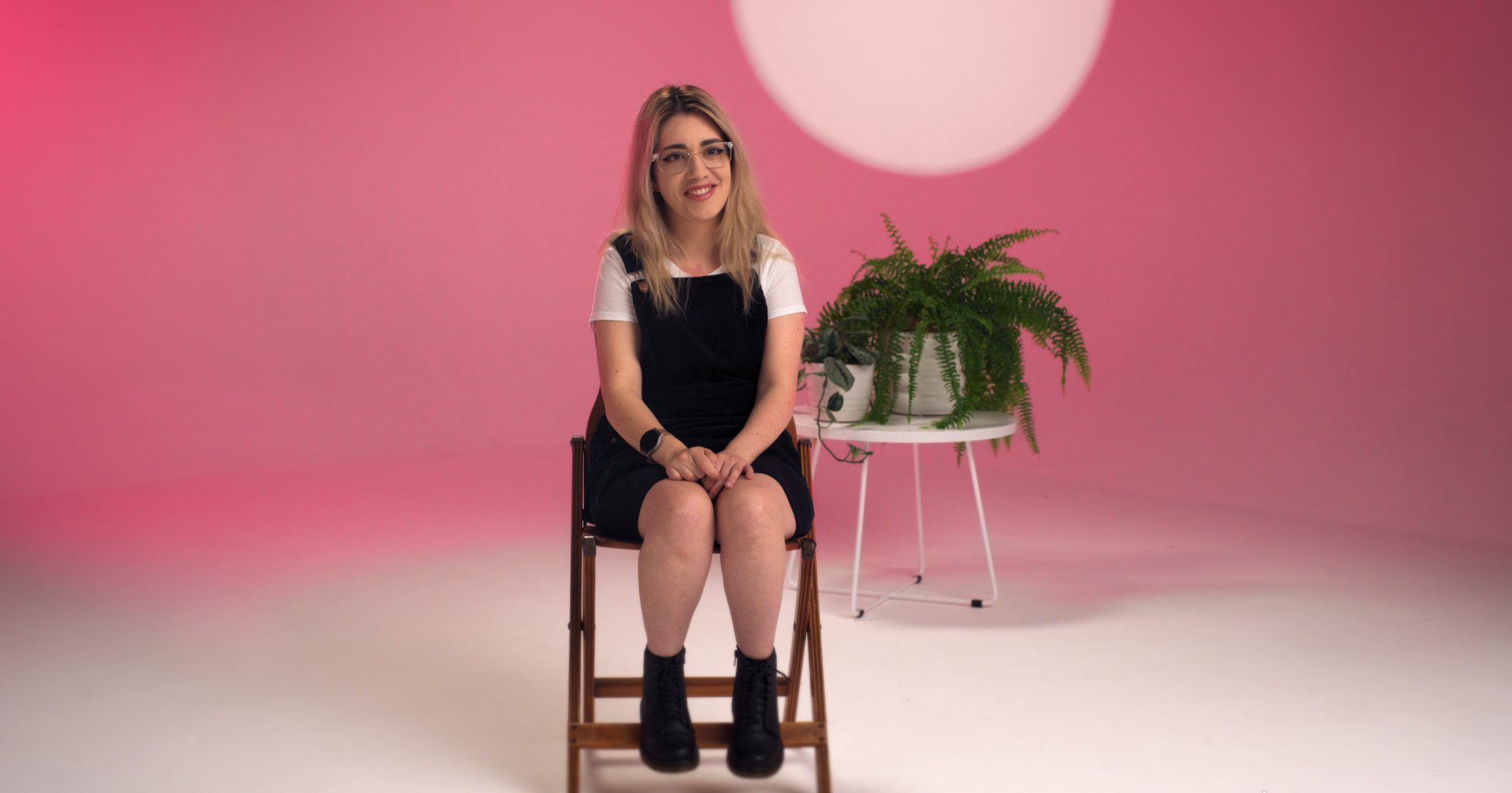 Gabriella Evans sits in a pink lit studio, smiling.