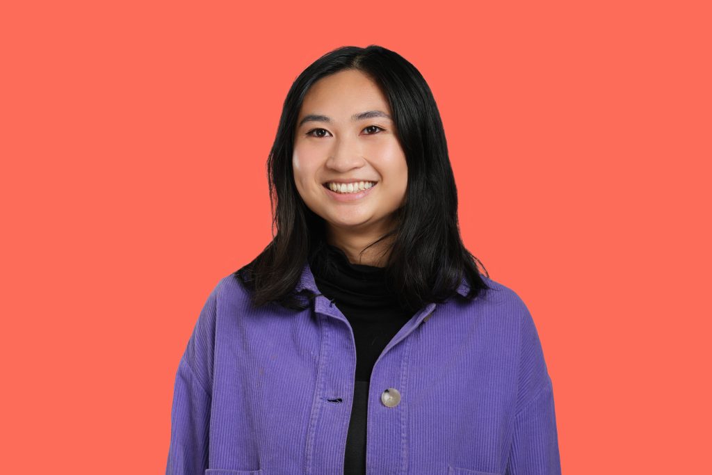 Jean Teng has shoulder length dark hair and a bright smile. She wears a purple jacket, and stands against an orange background